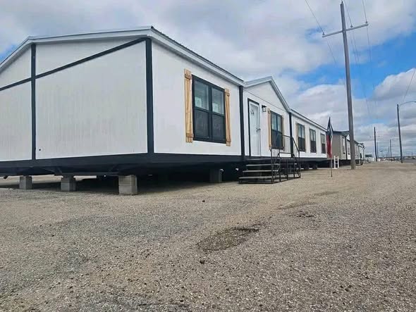 Modern luxury double-wide manufactured home for sale featuring a clean white siding exterior with contrasting black trim and rustic wooden shutters, a spacious open-concept interior with high-end wood-look flooring, a designer kitchen with a marble-patterned island, and a spa-like master bathroom with a black clawfoot soaking tub for a sophisticated 4-bedroom move-in ready turn-key residential design.