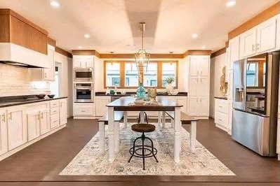 SEO-optimized alt text for a high-ranking luxury multi-section manufactured home kitchen featuring a professional gourmet interior design with an expansive central kitchen island and built-in farmhouse-style dining table; the bright, open-concept floor plan showcases premium white shaker-style cabinetry with warm wood-grain accents, a sophisticated stainless steel appliance suite including a French door refrigerator and double wall oven, and elegant pendant lighting, all set against high-end wide-plank flooring and a decorative area rug to highlight spacious double-wide mobile home floor plans, upscale modular kitchen decor, and luxury residential prefab home finishes for maximum search engine visibility and ranking.