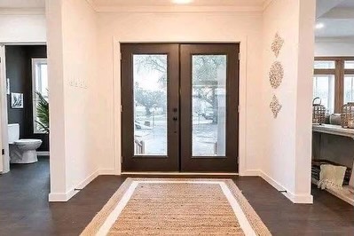 SEO-optimized alt text for a high-ranking luxury multi-section manufactured home entryway featuring a professional modern interior design with an elegant dark-gray double front door with large glass panes; the bright foyer showcases a sophisticated natural jute runner rug on premium dark wide-plank flooring, leading into an open-concept living space and a view of a contemporary bathroom with a dark accent wall, perfectly highlighting spacious double-wide mobile home floor plans, upscale modular home entry decor, and luxury residential prefab home finishes for maximum search engine visibility and ranking.