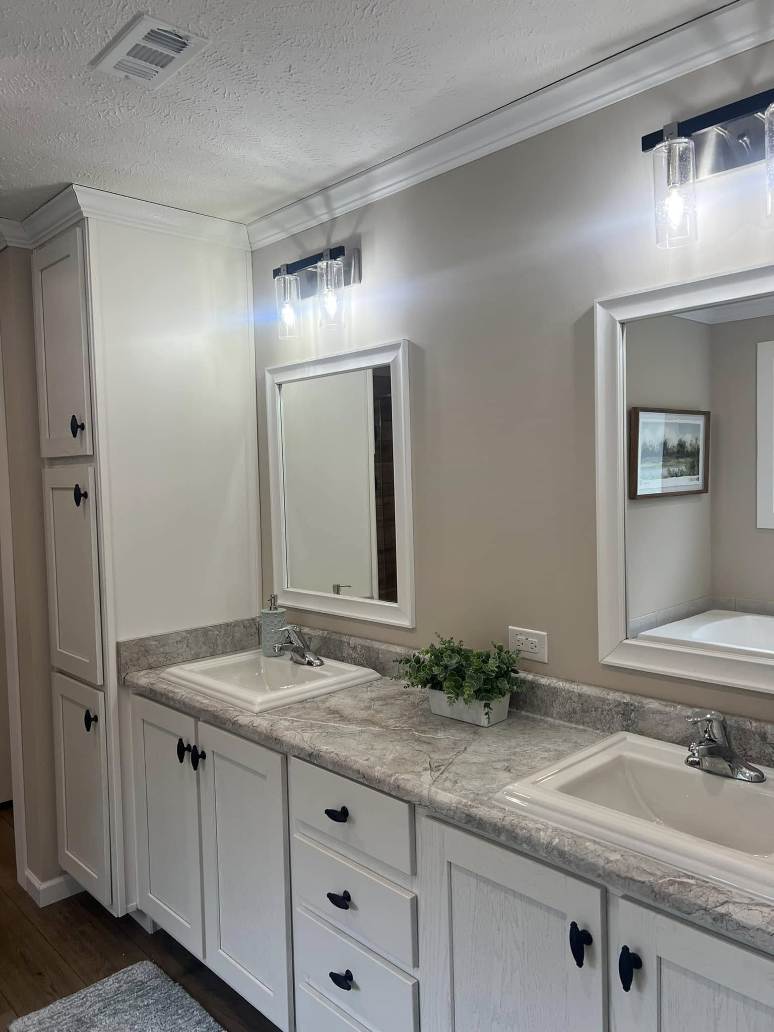 SEO-optimized alt text for a luxury manufactured home bathroom, featuring a double vanity with white shaker cabinets, elegant marble-look countertops, and dual integrated sinks with chrome faucets; the high-end interior design includes framed mirrors, modern glass pendant lighting, and a floor-to-ceiling linen cabinet, perfectly highlighting sophisticated mobile home master bath renovations and contemporary modular home floor plans for maximum search engine visibility and ranking.