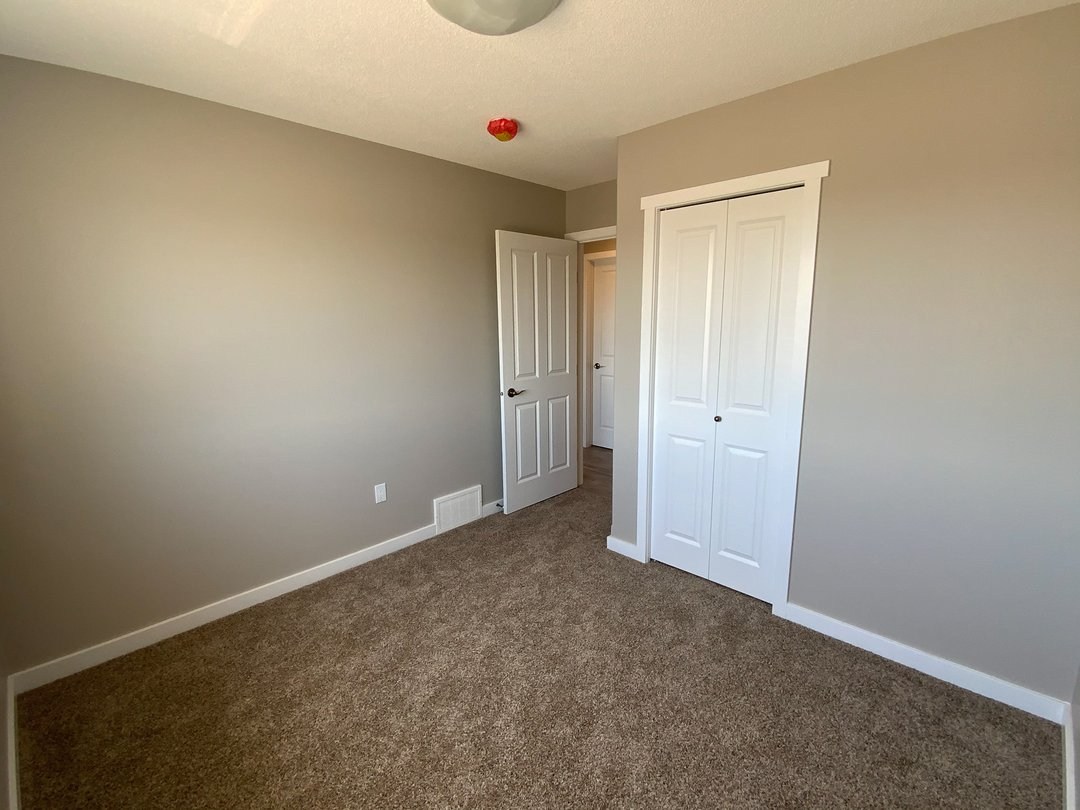 Modern luxury modular home interior featuring a spacious bedroom with neutral warm-toned walls and plush brown carpeting, showcasing a large white double-door built-in closet with clean trim and a matching white entry door for a high-end move-in ready turn-key residential property design.