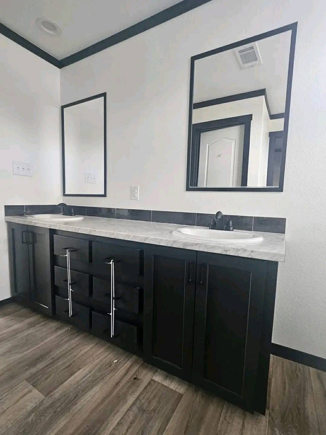 Modern luxury manufactured home interior featuring a spacious gourmet kitchen with white shaker cabinetry, a large marble-patterned island with seating, and a decorative tray ceiling with recessed lighting, transitioning into a cozy living room with plush grey sofas and neutral decor for a sophisticated 4-bedroom move-in ready turn-key residential design.