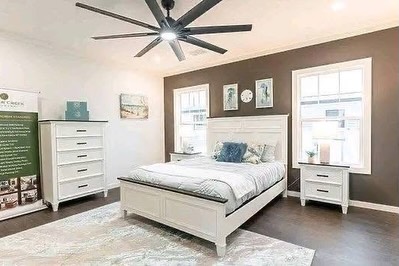 SEO-optimized alt text for a high-ranking luxury multi-section manufactured home master bedroom featuring a professional modern interior design with a sophisticated white and dark-gray color palette; the bright, spacious suite showcases a premium king-sized white bed frame with integrated dark-wood trim, matching white nightstands and a large five-drawer dresser, and a contemporary multi-blade ceiling fan, all set against a stylish dark-gray accent wall and high-end wide-plank flooring with a decorative area rug to highlight spacious double-wide mobile home floor plans, upscale modular bedroom decor, and luxury residential prefab home finishes for maximum search engine visibility and ranking. Would you like me to generate alt text for a different room in this luxury manufactured home?