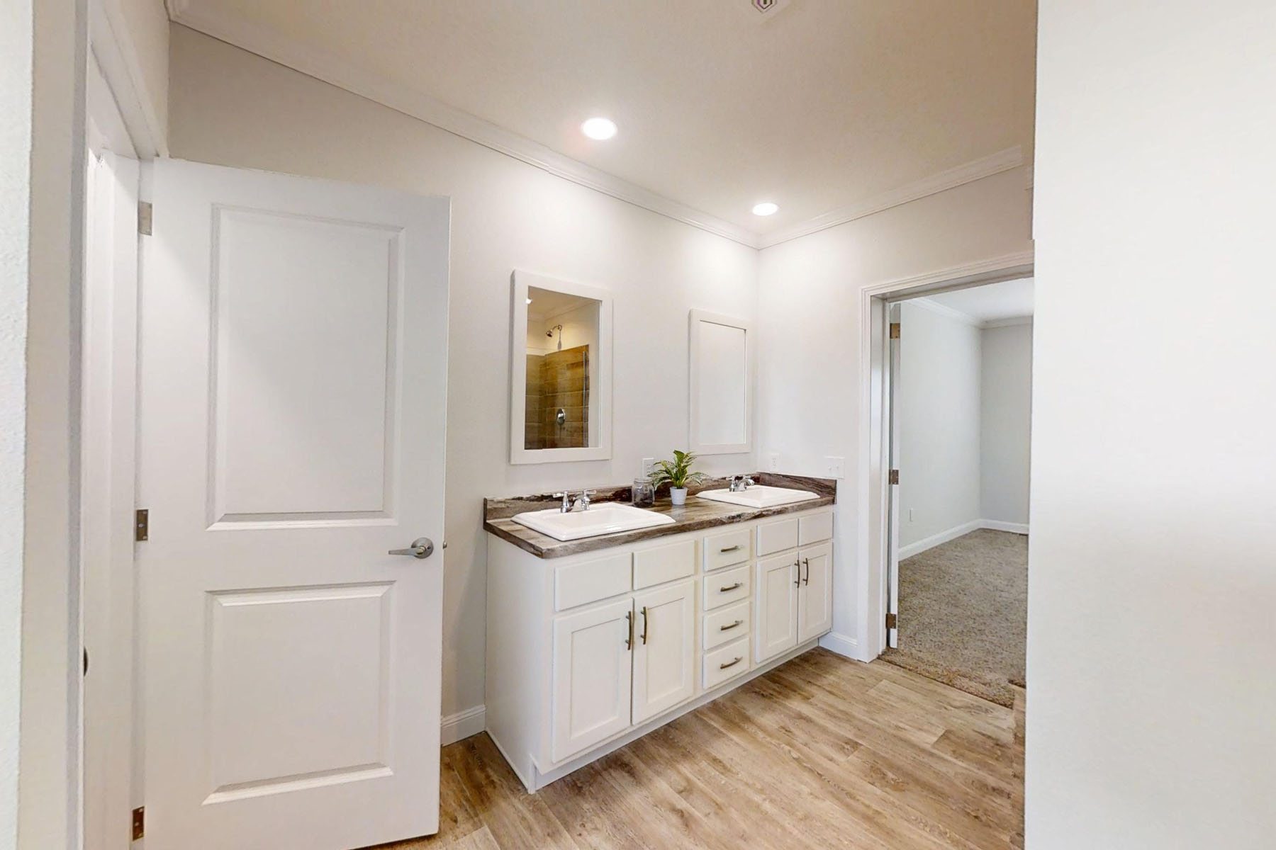 Modern galley kitchen interior in a manufactured home featuring white shaker-style cabinets, light wood butcher block countertops, a large porcelain farmhouse sink, and professional-grade stainless steel appliances including a gas range and chimney vent hood, all set on durable light oak laminate flooring for a clean, contemporary open-concept home design.