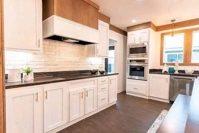 SEO-optimized alt text for a high-ranking luxury multi-section manufactured home kitchen featuring a professional gourmet interior design with a sophisticated white and wood-tone aesthetic; the bright, open-concept floor plan showcases premium white shaker-style cabinetry with warm wood headers, high-end stainless steel appliances including a built-in double wall oven and French door refrigerator, and a sleek black quartz countertop with a classic white subway tile backsplash, perfectly highlighting spacious double-wide mobile home floor plans, upscale modular kitchen decor, and luxury residential prefab home finishes for maximum search engine visibility and ranking.