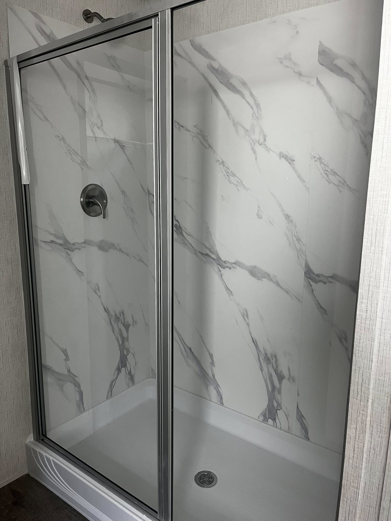 SEO-optimized alt text for a high-ranking, modern master bathroom in a luxury manufactured home featuring a walk-in shower with elegant white marble-patterned wall panels and a sleek silver-framed glass door; the professional interior design showcases contemporary plumbing fixtures and clean lines, perfectly highlighting premium mobile home bathroom floor plans, stylish modular home shower upgrades, and sophisticated residential master suite renovations for maximum search engine visibility and ranking.