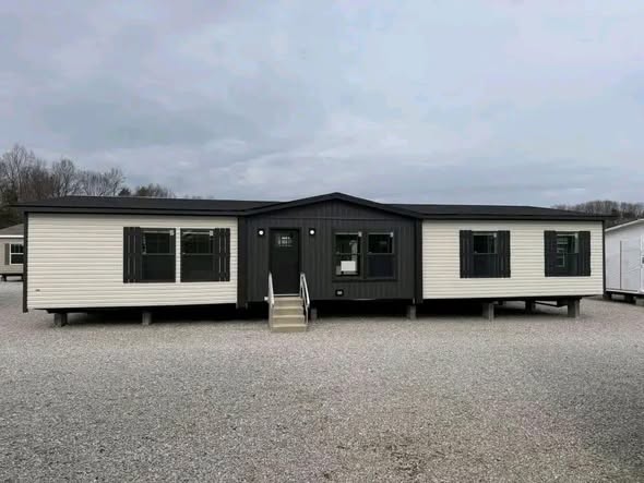 Modern luxury double-wide manufactured home for sale featuring a contemporary charcoal grey and white horizontal siding exterior with matching dark shutters, a central gabled entryway with a white concrete staircase on a professional block foundation, and an expansive 4-bedroom floor plan designed for high-end affordable residential living in a turn-ready property.
