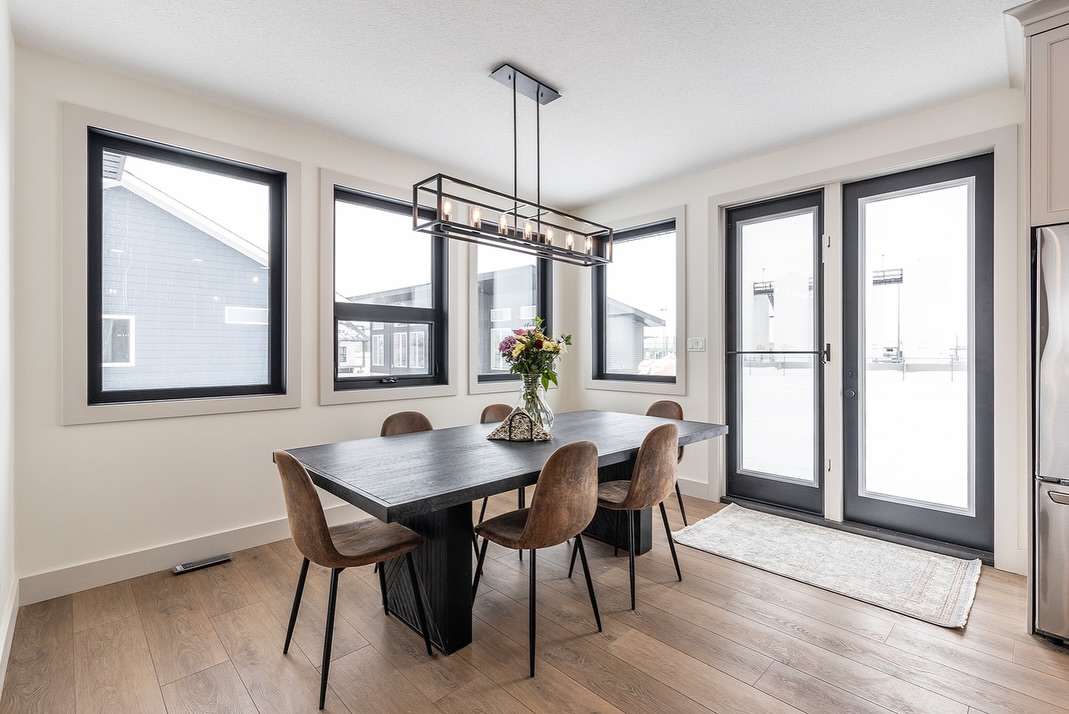 SEO-optimized alt text for a high-ranking luxury custom modular home dining room featuring a professional open-concept interior design with a sleek black rectangular dining table and stylish brown leather chairs; the architectural view showcases premium black-framed windows and matching French doors that flood the space with natural light, complemented by a contemporary black linear cage chandelier with Edison bulbs and durable wide-plank oak flooring, perfectly highlighting gourmet prefab home floor plans, modern craftsman-style architectural details, and high-end residential mobile living solutions for maximum search engine visibility and ranking.

Would you like me to generate a description for the living room or the exterior of this home next?