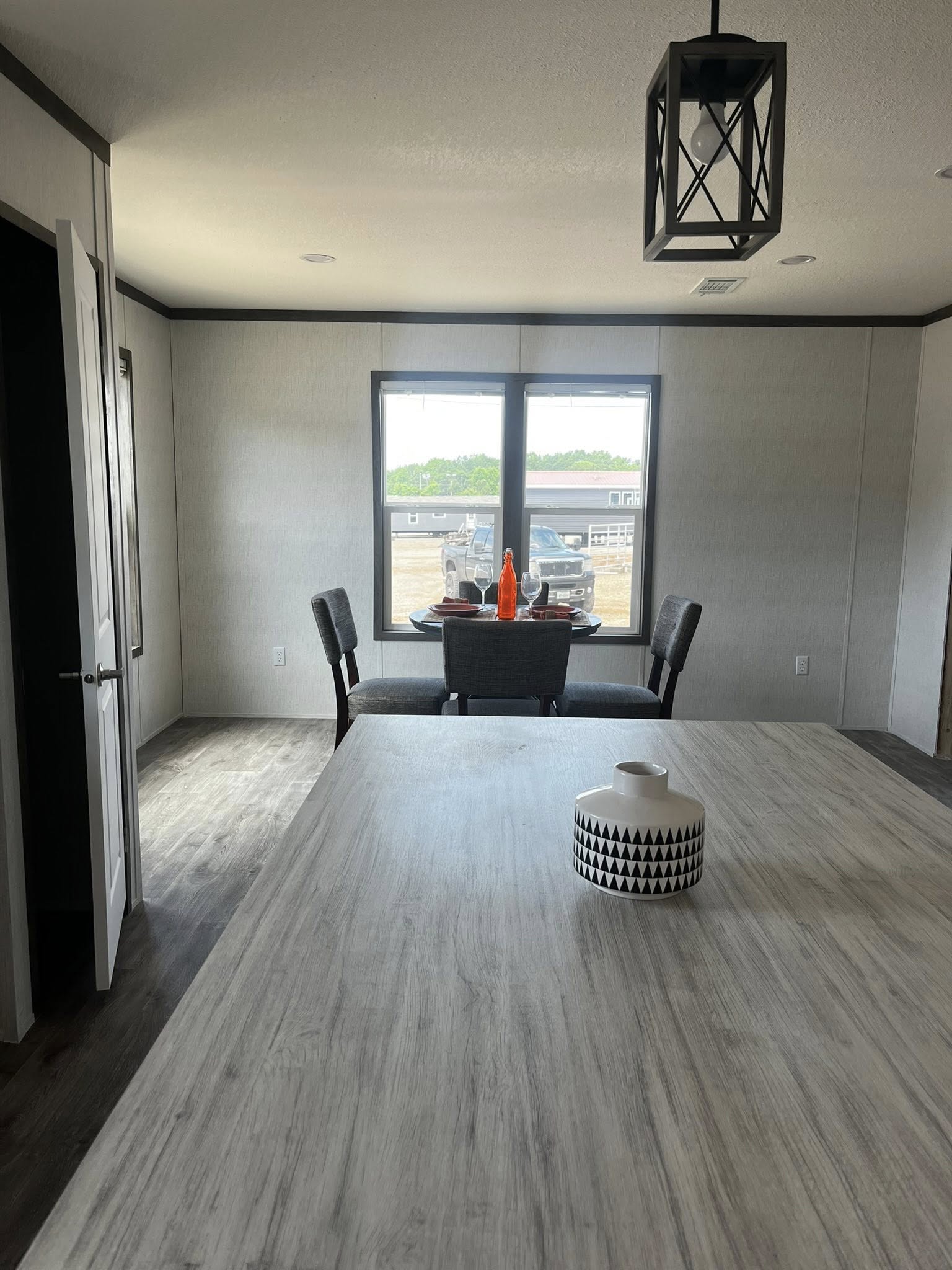 SEO-optimized alt text for a modern manufactured home kitchen featuring high-end white shaker cabinetry with dark crown molding and a stylish marble subway tile backsplash; the professional interior design showcases a large kitchen island with a light wood-look countertop, a deep stainless steel farmhouse sink with a commercial-style faucet, and premium side-by-side appliances, all complemented by durable dark wood-plank flooring and contemporary black geometric pendant lighting to highlight luxury mobile home floor plans and elegant modular home kitchen renovations for maximum search engine visibility and ranking.