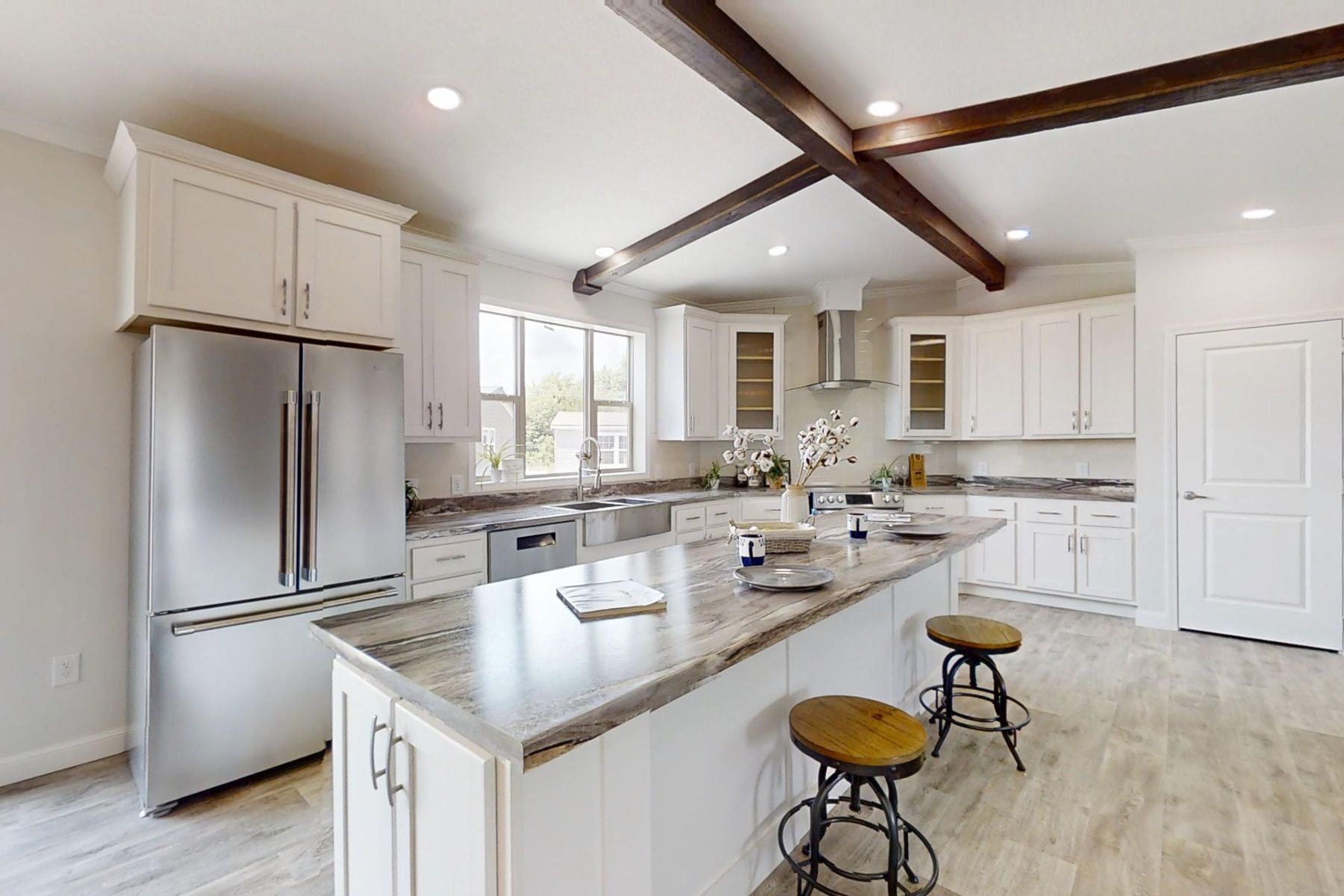 Modern transitional kitchen and living room design featuring a white double-bowl farmhouse sink with a brushed nickel gooseneck faucet, light oak butcher block countertops, and white shaker cabinets, seamlessly transitioning into an open-concept living space with neutral decor, a striped accent chair, and large windows for a bright and airy home interior inspiration.
