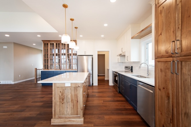 SEO-optimized alt text for a high-ranking luxury custom modular home kitchen featuring a professional open-concept interior design with a striking navy blue and rustic wood cabinetry combination; the architectural view showcases a large wood-plank kitchen island with a white quartz countertop, a grand floor-to-ceiling glass-front hutch, and premium stainless steel appliances, all complemented by elegant white shaker upper cabinets, a classic subway tile backsplash, and contemporary gold pendant lighting set against rich dark wide-plank hardwood flooring, perfectly highlighting gourmet prefab kitchen layouts, modern craftsman-style architectural details, and high-end residential mobile living solutions for maximum search engine visibility and ranking.