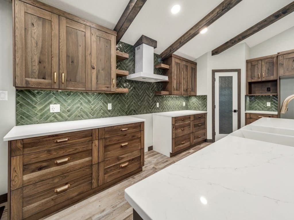 A luxury modern rustic kitchen featuring dark wood cabinets, a striking green herringbone tile backsplash, white quartz countertops, and exposed wooden ceiling beams for a warm, sophisticated interior design.