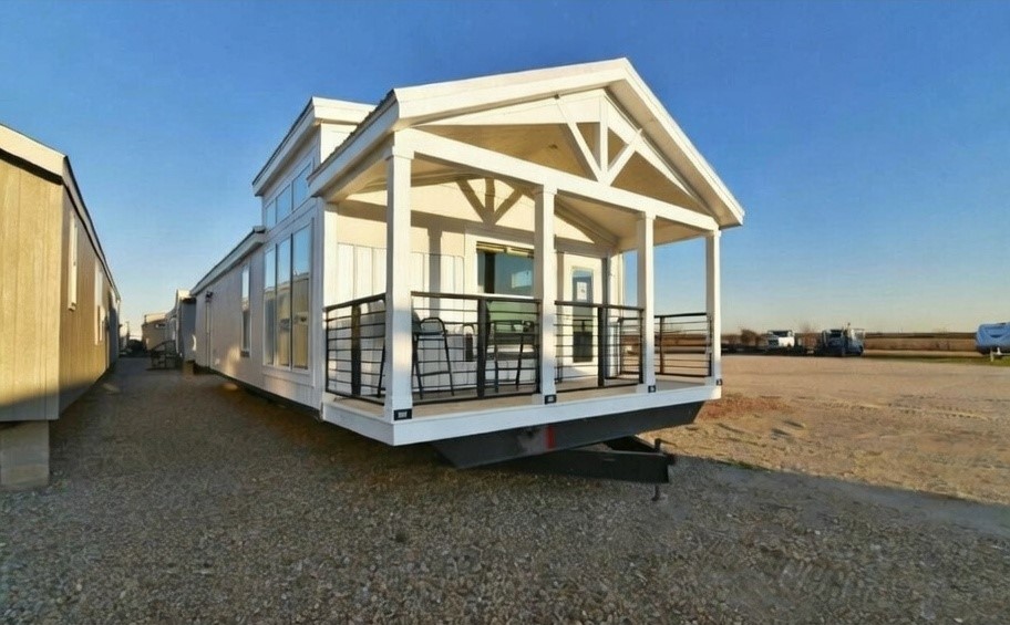 SEO-optimized alt text for a high-ranking luxury custom park model tiny home exterior featuring a professional architectural design with a grand covered front porch and vaulted gabled roofline; the view showcases a modern white prefab residence with energy-efficient oversized windows, a contemporary black metal railing, and high-end vertical siding, perfectly highlighting premium small-space living floor plans, upscale tiny house curb appeal, and luxury residential mobile home finishes for maximum search engine visibility and ranking.