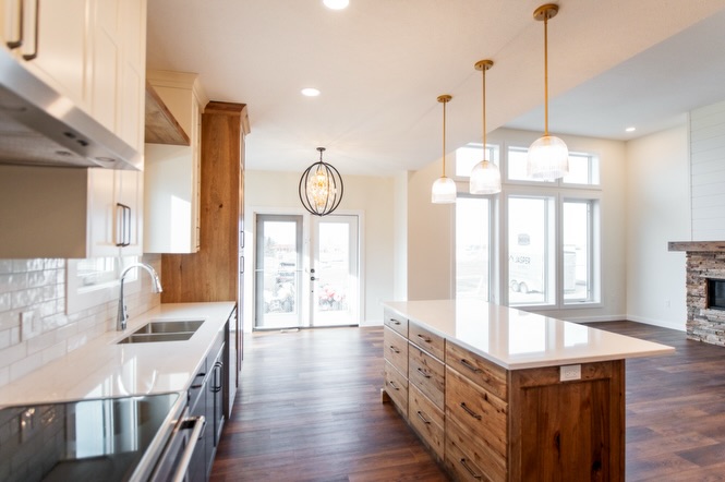 SEO-optimized alt text for a high-ranking luxury custom modular home kitchen and dining area featuring a professional open-concept interior design with a massive white quartz waterfall island and rustic wood cabinetry; the architectural view showcases a sophisticated navy blue kitchen base with a grand floor-to-ceiling glass-front hutch, premium stainless steel KitchenAid appliances, and elegant white upper cabinets, complemented by contemporary frosted glass globe pendant lighting and a chic black orb chandelier over a bright dining space with large white-framed windows, all set against rich dark wide-plank hardwood flooring to highlight gourmet prefab kitchen layouts, modern craftsman-style architectural details, and high-end residential mobile living solutions for maximum search engine visibility and ranking.