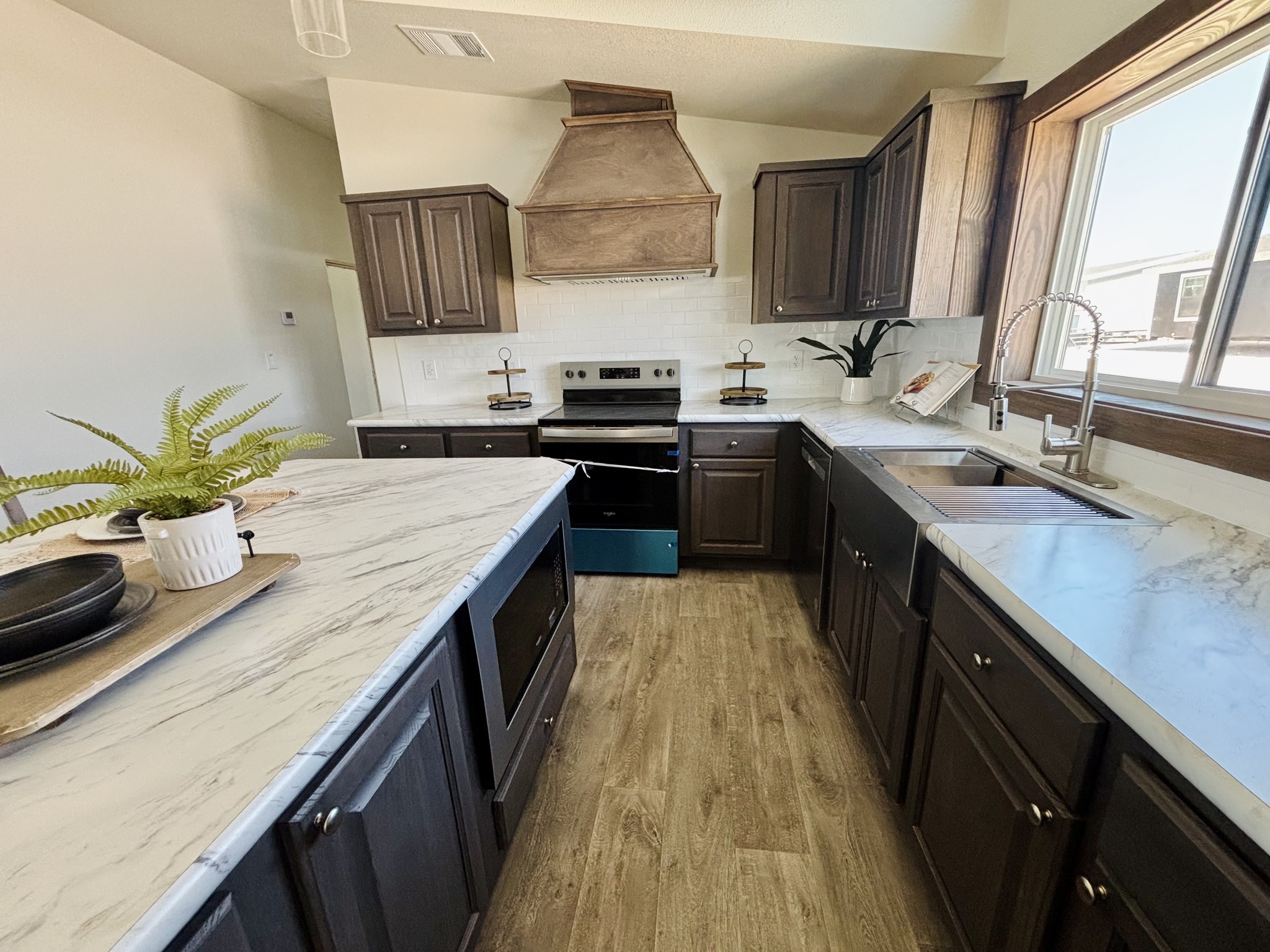 Spacious kitchen with dark wood cabinets, marble countertops, and a central island. Stainless steel appliances and a large window create a bright, modern feel.