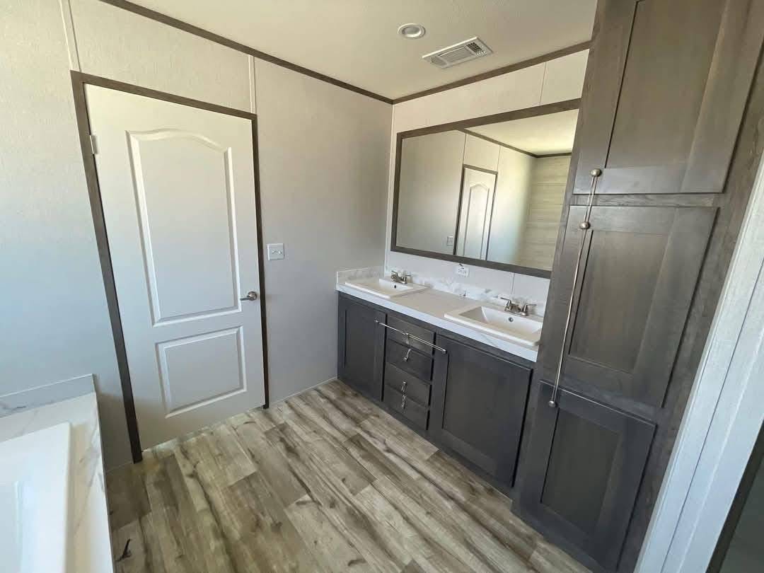 Modern bathroom interior with double-sink vanity, dark wood cabinetry, large mirror, white countertop, tall storage cabinet, wood-look flooring, marble-patterned bathtub surround, and contemporary clean design perfect for home decor, interior design inspiration, and real estate listings.