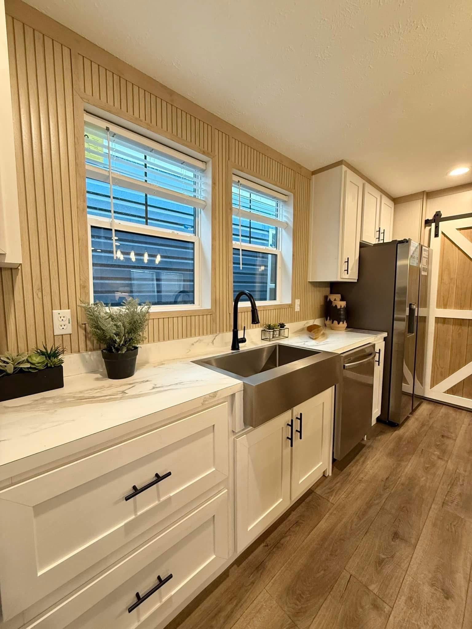 Modern luxury farmhouse kitchen featuring sleek white shaker cabinets with black hardware, a large marble-patterned island with integrated breakfast bar seating, and high-end stainless steel appliances, all set against a unique vertical wood-slat backsplash and warm wide-plank flooring for a sophisticated 4-bedroom move-in ready turn-key residential design.