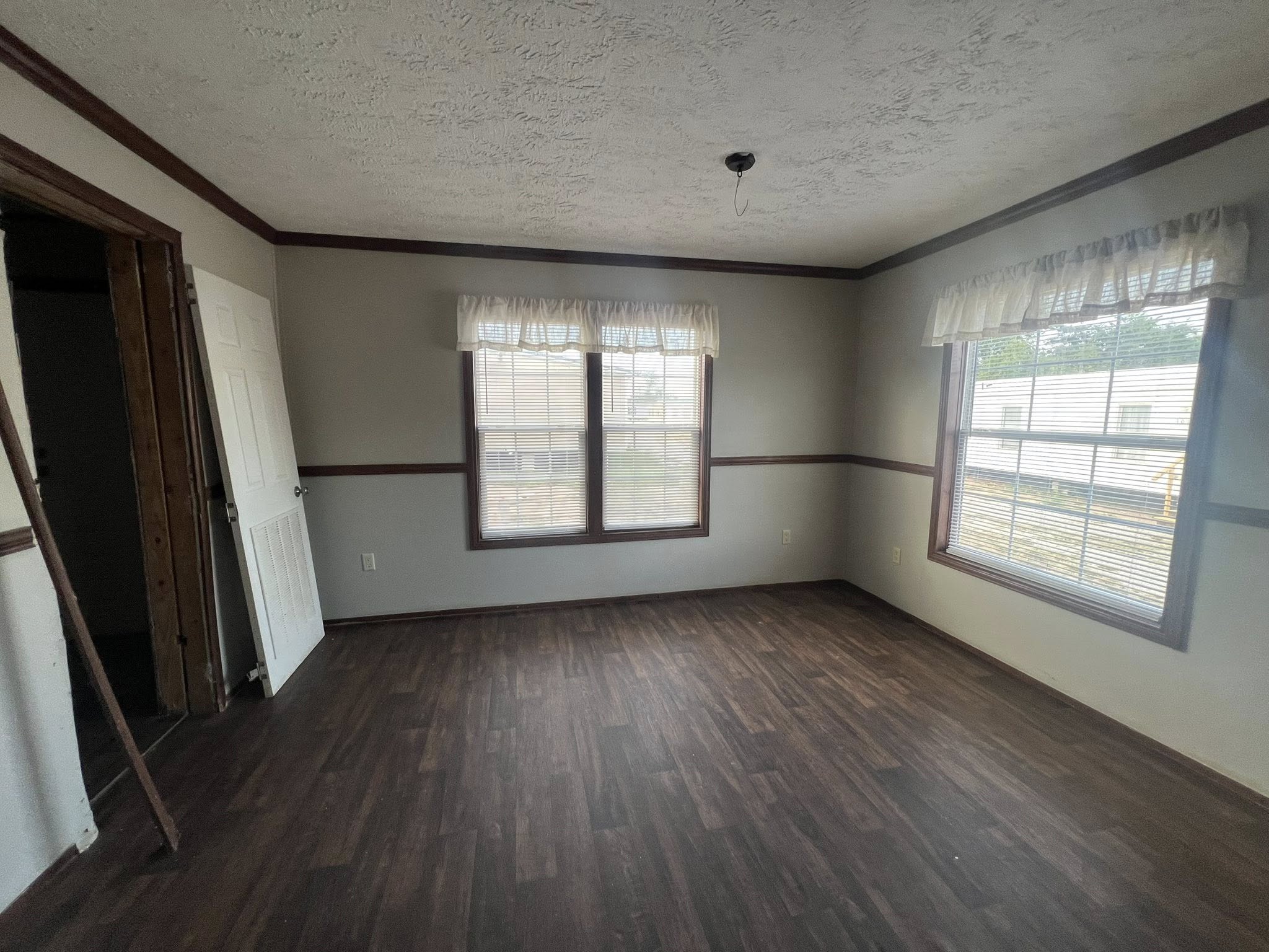 SEO-optimized alt text for a spacious, traditional double-wide manufactured home living room featuring neutral gray carpeting and a classic brick-surround fireplace with a wooden mantel; the high-ranking interior design showcases dark wood built-in bookshelves, a large round wall clock, and a central ceiling fan, all framed by elegant dark crown molding and floral-patterned curtains that highlight comfortable family-style modular home floor plans and affordable luxury mobile home decor for maximum search engine visibility and ranking.