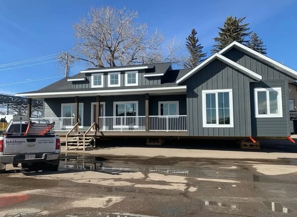 SEO-optimized alt text for a high-ranking modern luxury modular home featuring a professional dark slate gray board-and-batten exterior with crisp white trim and a spacious integrated front porch; the architectural view showcases a high-quality prefab residence with a complex gabled roofline, energy-efficient white-framed windows, and a secure elevated foundation, perfectly highlighting premium manufactured home curb appeal, contemporary residential floor plans, and upscale durable construction for maximum search engine visibility and ranking.