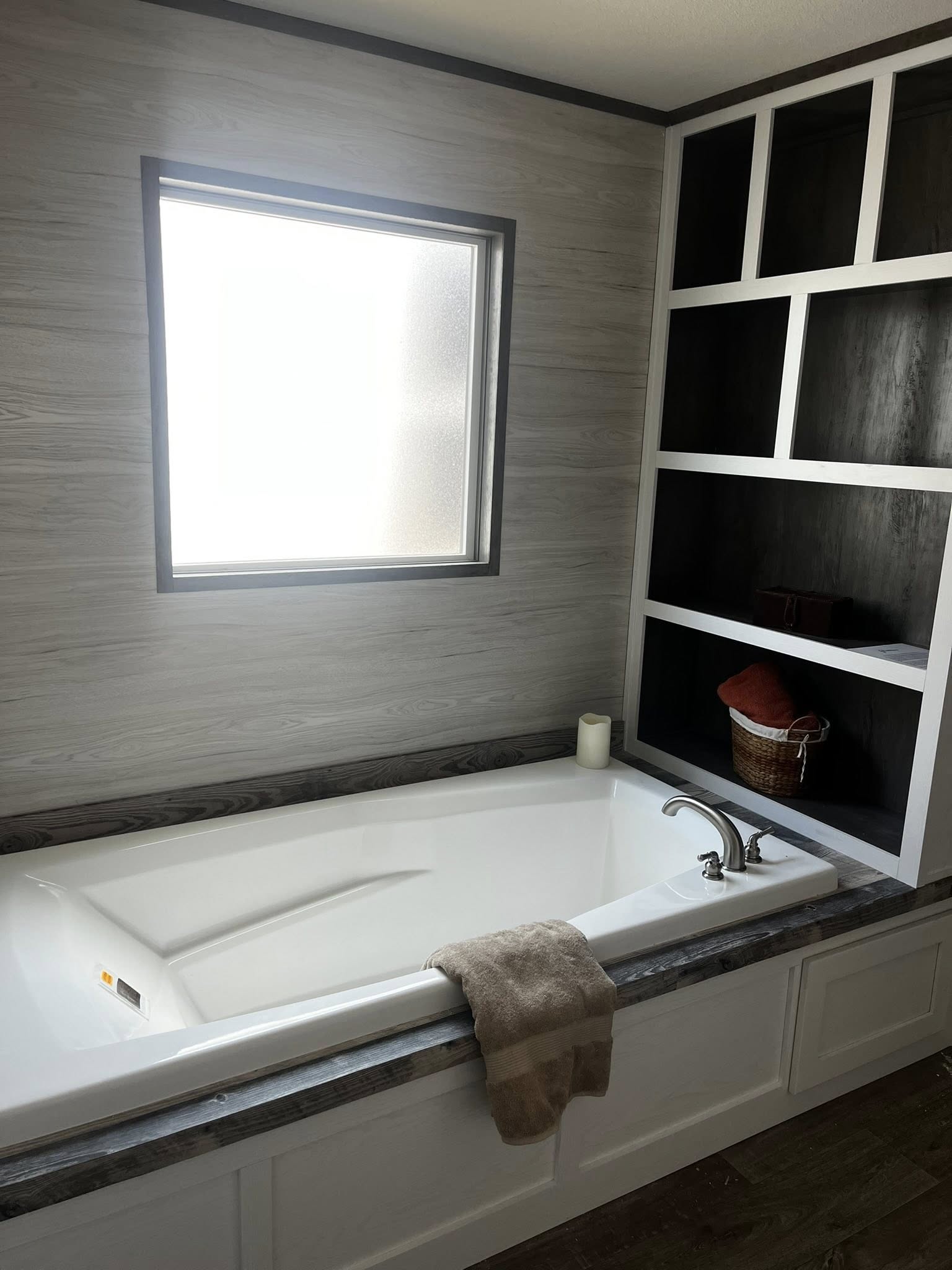 
Gemini said
SEO-optimized alt text for a high-ranking master bathroom in a modern manufactured home featuring a large white soaking tub with a silver faucet and a dark wood-look surround; the professional interior design showcases a built-in black and white open shelving unit for storage, light gray wood-grain wall panels, and a frosted privacy window that provides soft natural light, perfectly highlighting luxury mobile home master suite floor plans, contemporary modular home bathroom features, and stylish residential renovation ideas for maximum search engine visibility and ranking.