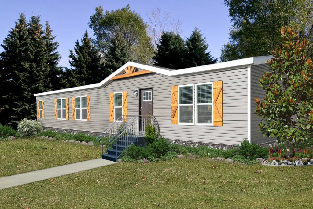 SEO-optimized alt text for a modern double-wide manufactured home featuring light gray horizontal vinyl siding, rustic wood-look board and batten shutters, and a decorative wooden gable accent over the front entrance; the residential exterior showcases a dark brown front door with glass panes, a sturdy metal staircase, and professional landscaping with a brick-patterned foundation skirt, perfectly highlighting high-end mobile home curb appeal, contemporary modular home designs, and premium manufactured housing floor plans for maximum search engine visibility and ranking.