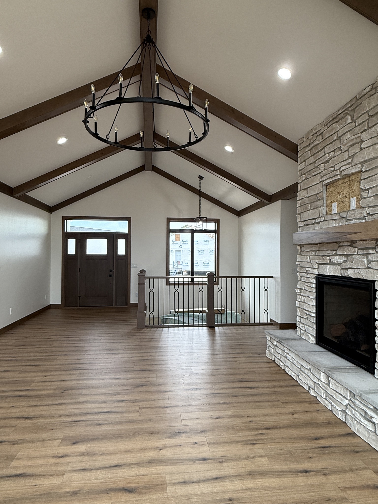 SEO-optimized alt text for a high-ranking modern luxury modular home interior featuring a spacious, open-concept living area with vaulted ceilings and rustic dark wood beams; the professional interior design showcases a grand floor-to-ceiling stone-veneer fireplace with a thick wood mantel, a sophisticated black wrought-iron wagon wheel chandelier, and durable wide-plank oak flooring, perfectly highlighting premium prefab home floor plans, contemporary craftsman-style architectural details, and high-end residential mobile living solutions for maximum search engine visibility and ranking.

Would you like me to describe the modern exterior or the entryway of this luxury modular home next?