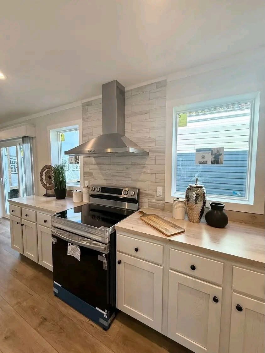 
Gemini said
Modern open-concept kitchen and living area featuring white shaker cabinets, light oak butcher block countertops, a double-bowl farmhouse sink, and stainless steel appliances, seamlessly transitioning into a bright living room with dark wood ceiling beams, neutral grey furniture, and a stone fireplace, creating a cohesive transitional home interior design perfect for modern family living and home renovation inspiration.