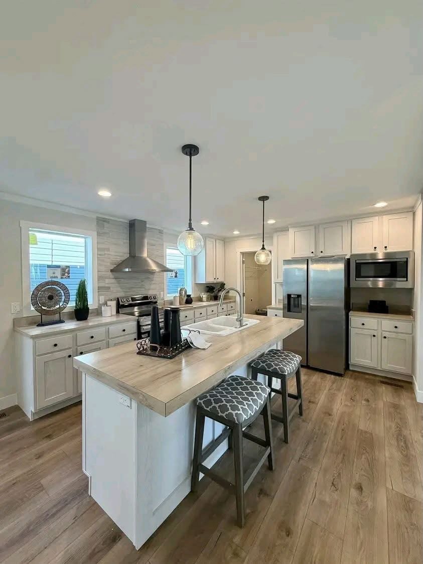 
Gemini said
Modern open-concept home interior featuring a bright galley kitchen with white shaker cabinets, light oak butcher block countertops, a large porcelain farmhouse sink, and premium stainless steel appliances, seamlessly flowing into a spacious living room with dark wood ceiling beams, neutral grey furniture, a floral area rug, and a stone fireplace, creating a cohesive and stylish transitional living space ideal for modern family home inspiration.