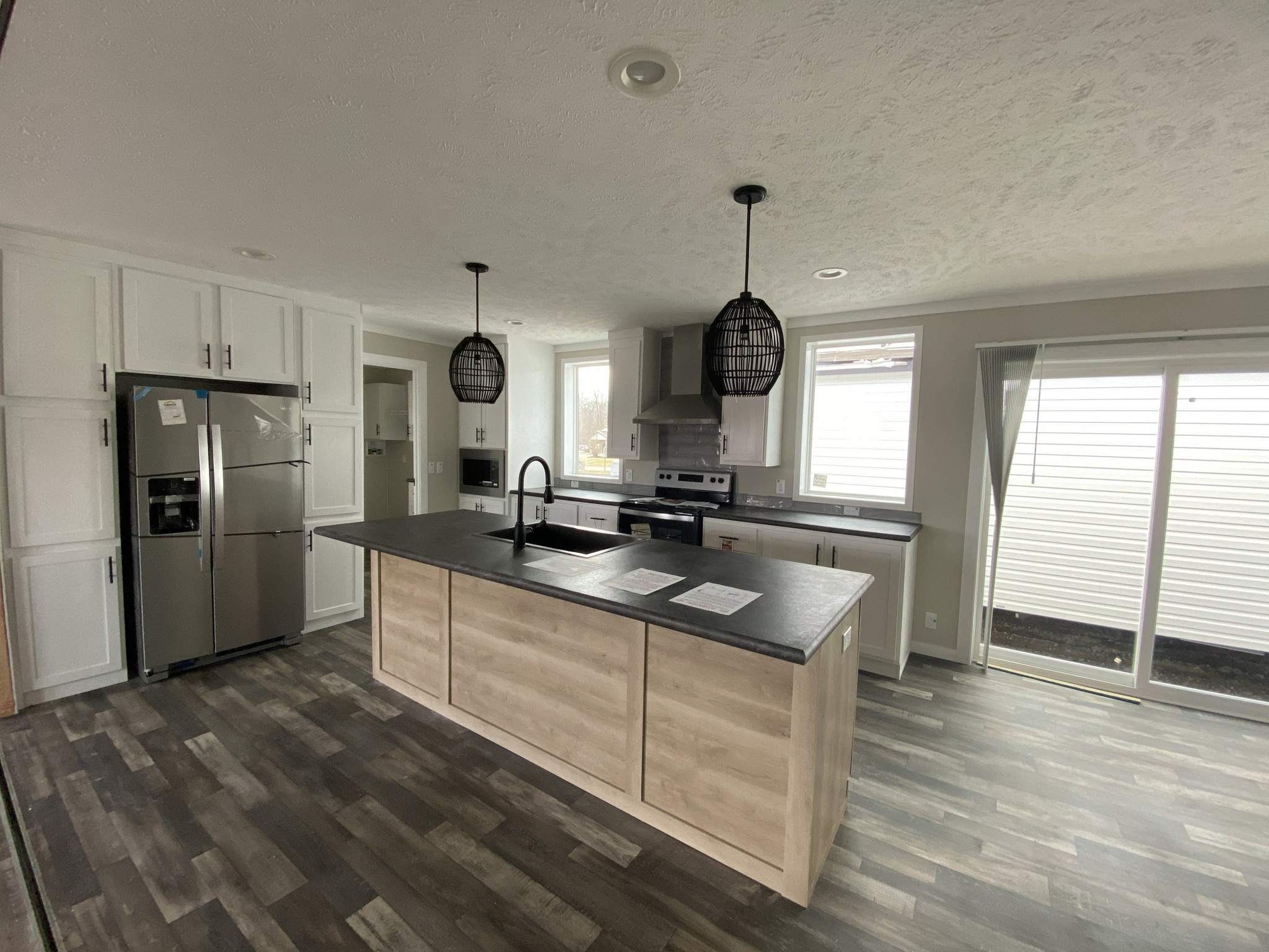 Modern kitchen with gray wood flooring, light wood island, and black countertop. Stainless steel appliances and hanging lights create a sleek ambiance.