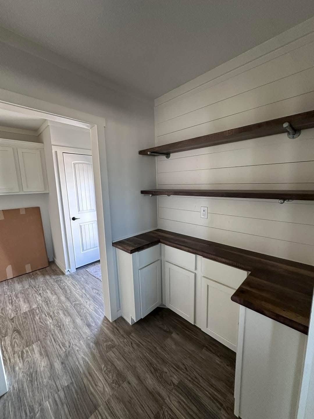 Modern farmhouse laundry room and butler's pantry design featuring white shaker cabinets, dark walnut butcher block countertops, and rustic floating wood shelves mounted on a white shiplap accent wall with industrial pipe brackets and durable wood-look laminate flooring.