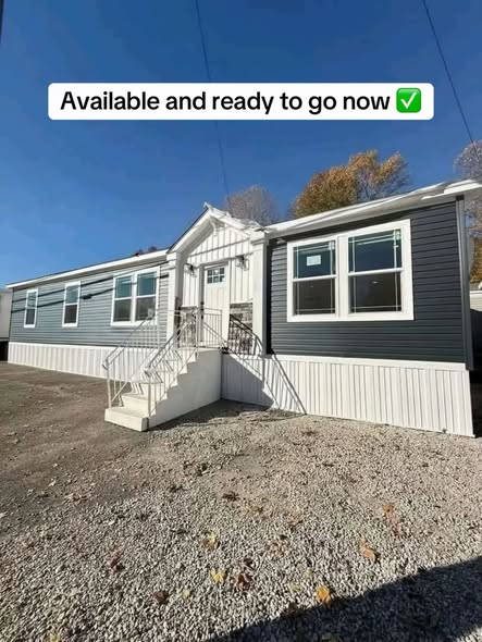 SEO-optimized alt text for a high-ranking luxury multi-section manufactured home exterior featuring a professional architectural design with charcoal gray horizontal lap siding and a bright white vertical board-and-batten entryway; the modern facade showcases energy-efficient white-trimmed windows, a clean white skirting foundation, and a welcoming front porch with white railings and steps, perfectly highlighting spacious double-wide mobile home floor plans, upscale contemporary curb appeal, and high-end residential prefab home construction for maximum search engine visibility and ranking.