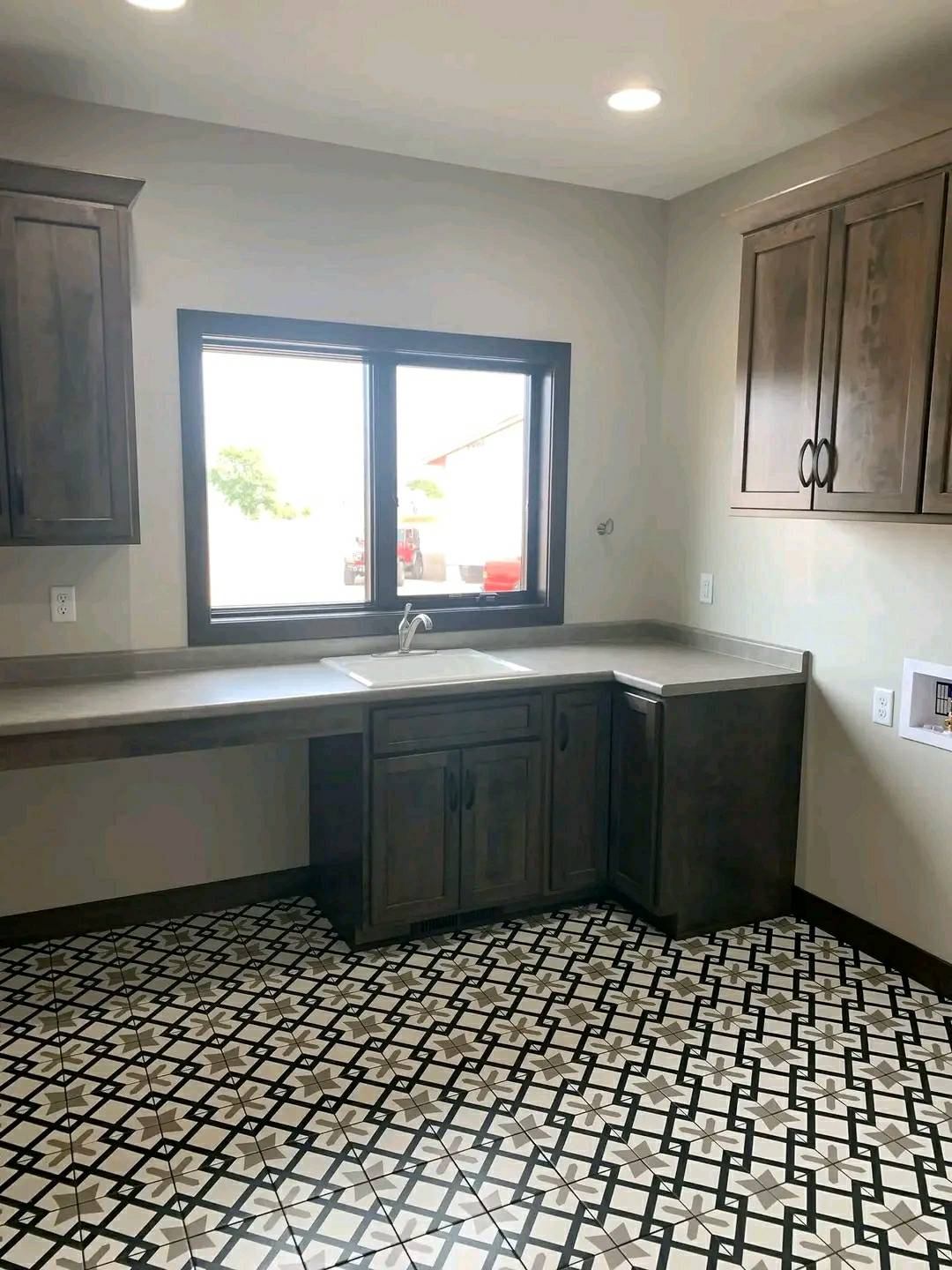 A kitchen with a geometric tiled floor, dark wooden cabinets, and a large window above the sink. The space is clean and bright, creating a modern feel.