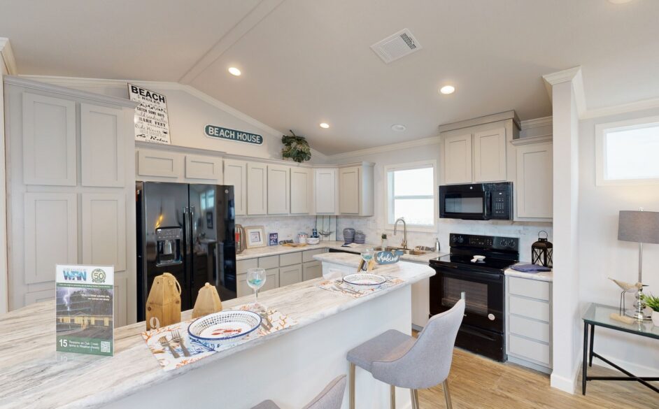 Modern kitchen with cream cabinets, black appliances, and a marble countertop. Decor includes beach-themed signs and place settings for two. Cozy and inviting atmosphere.