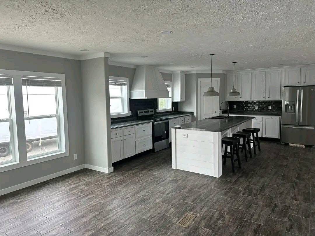 Modern kitchen with gray tones featuring a large island with stools, stainless steel appliances, white cabinets, and pendant lighting, creating a sleek, inviting atmosphere.