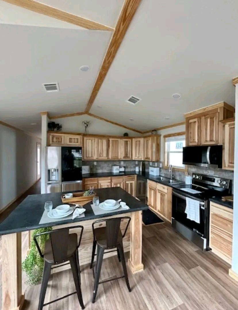 Spacious kitchen with light wood cabinets, dark countertops, and stainless steel appliances. A small island with two chairs and set tableware adds warmth.