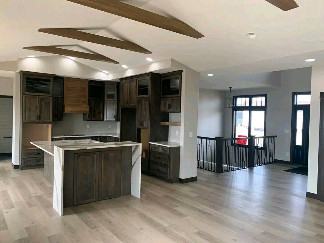 Modern kitchen with dark wood cabinets, light countertops, and a large island. Beamed ceiling and spacious open layout create an airy, welcoming feel.