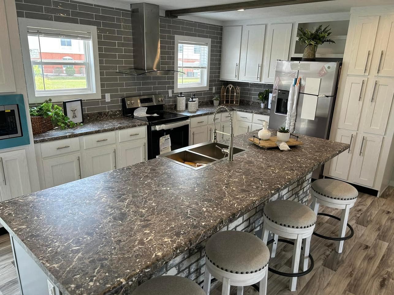 Spacious kitchen with gray tile backsplash, white cabinets, and stainless steel appliances. A large marble island with beige stools enhances the cozy, modern vibe.
