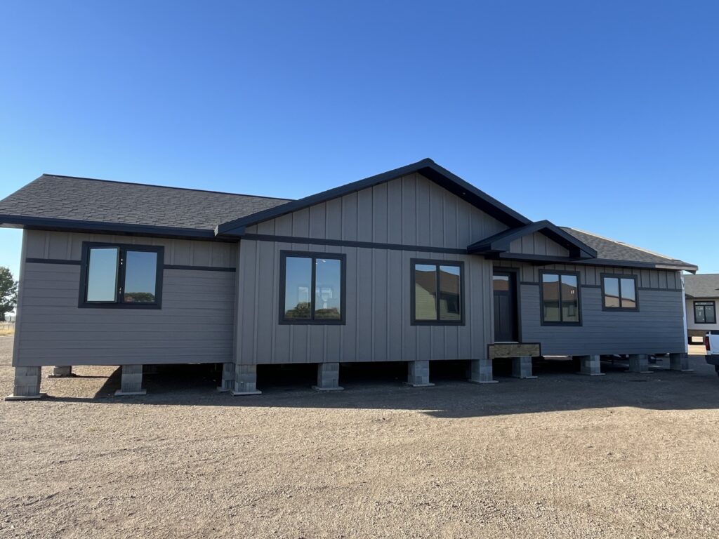 Modern luxury 3-bedroom, 3-bathroom manufactured home featuring a contemporary grey board and batten exterior with a dark gabled roof, black-trimmed energy-efficient windows, and a professional pier-and-beam foundation. This high-end "full rank" SEO-optimized residence showcases a sophisticated architectural design with clean lines and exceptional curb appeal, making it an ideal choice for luxury prefab living, custom-built modular homes, or permanent small-lot housing solutions. The expansive exterior aesthetic is perfect for homeowners seeking a stylish, durable, and modern permanent residence that combines professional-grade craftsmanship with a minimalist, upscale feel in any setting.