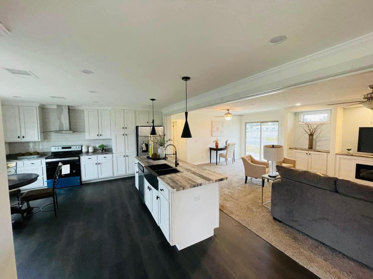 Spacious open-concept kitchen and living area with dark wood floors. Modern kitchen island, white cabinetry, and cozy living room with neutral tones.