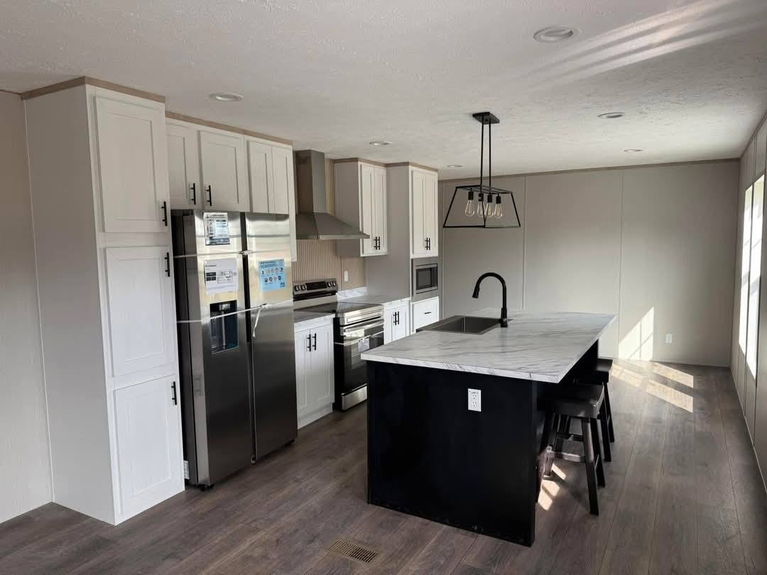 Modern kitchen with white cabinets and a marble island, featuring stainless steel appliances. The room is spacious and bright with natural light.