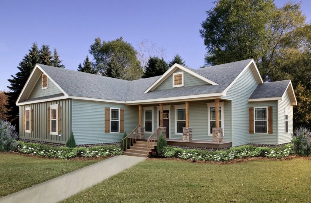 A charming, light green single-story house with a gabled roof, a welcoming porch, and wooden accents surrounded by well-kept lawn and trees under a clear sky.