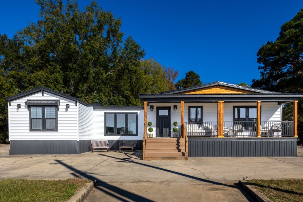 Single-story house with a gray and white exterior, a front porch with wooden columns, and steps leading to a dark door. Large trees are in the background.