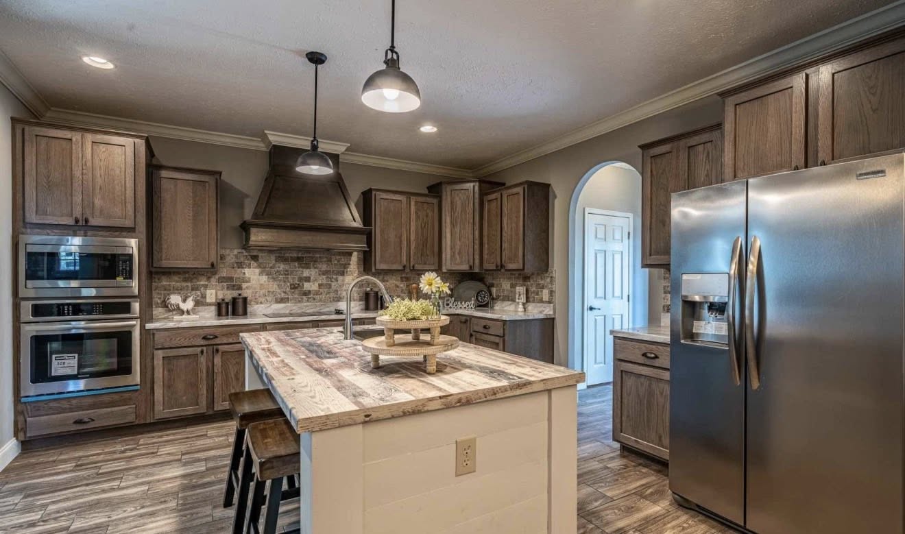 Spacious kitchen with rustic charm, featuring wooden cabinets, a large island with stools, stainless steel appliances, and warm lighting.