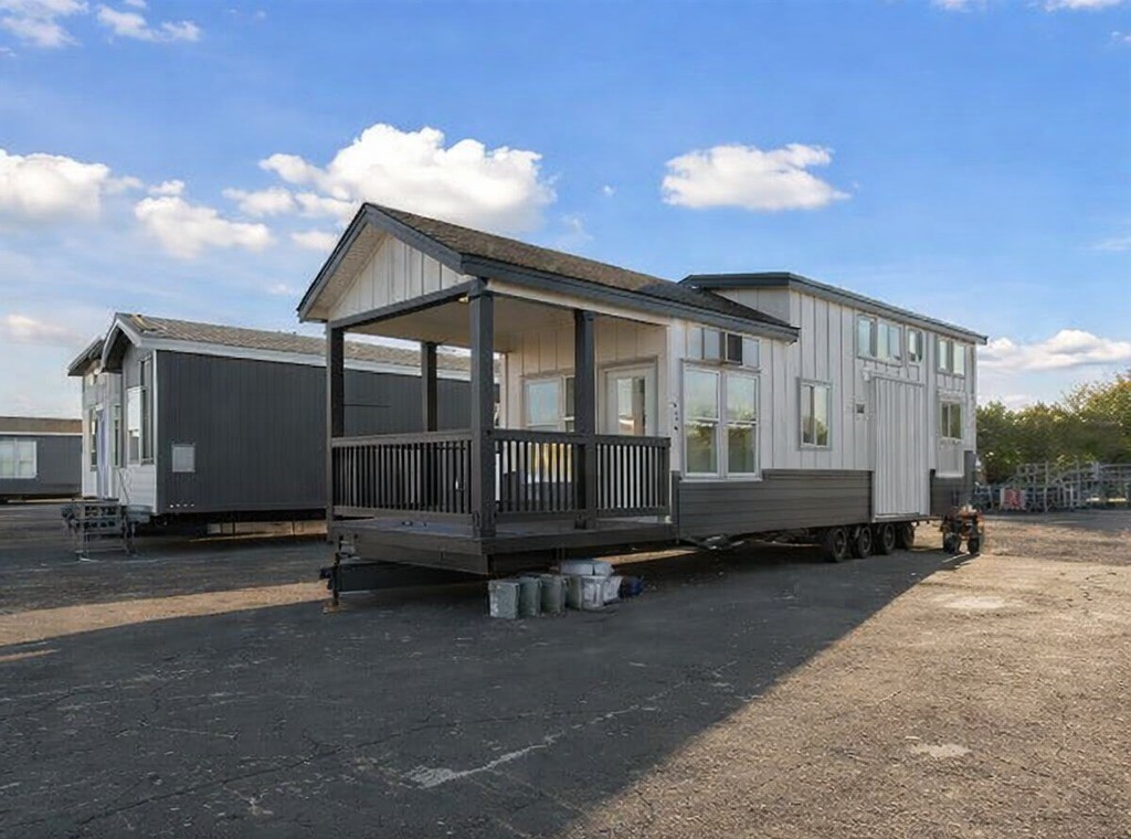 Gemini said Modern luxury tiny house on wheels featuring a two-tone white board and batten and dark charcoal siding, a large covered front porch with black railings, and multiple clerestory windows for ample natural light. This professional park model cottage design by Recreational Resort Cottages showcases a high-end mobile lifestyle, combining a spacious outdoor deck area with a contemporary architectural aesthetic, perfect for SEO-targeted searches regarding luxury tiny homes, portable guest houses, and upscale vacation rentals.