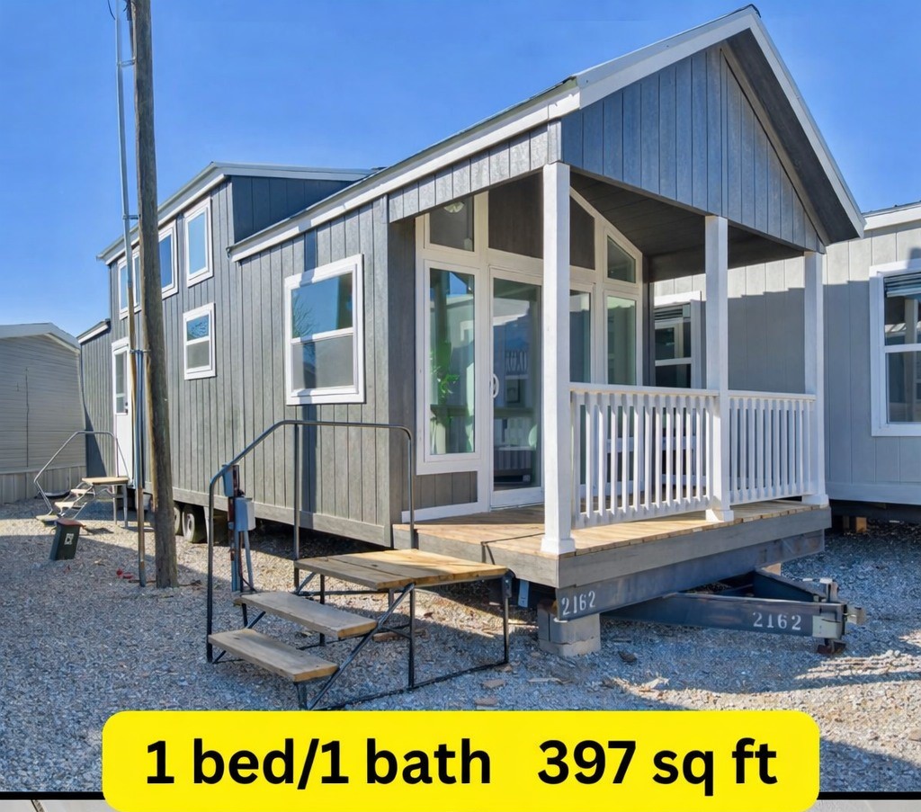 Modern luxury 1-bedroom, 1-bathroom park model tiny home for sale featuring 397 square feet of living space, a sophisticated grey vertical board and batten exterior, and a stunning gabled front porch with white railings and pillars. The high-end architectural design includes a multi-level roofline with energy-efficient clerestory windows, a secondary side entrance, and a portable multi-axle chassis, making it an ideal "full rank" SEO-optimized solution for premium prefab living, custom backyard accessory dwelling units (ADU), or a luxury vacation cabin retreat.