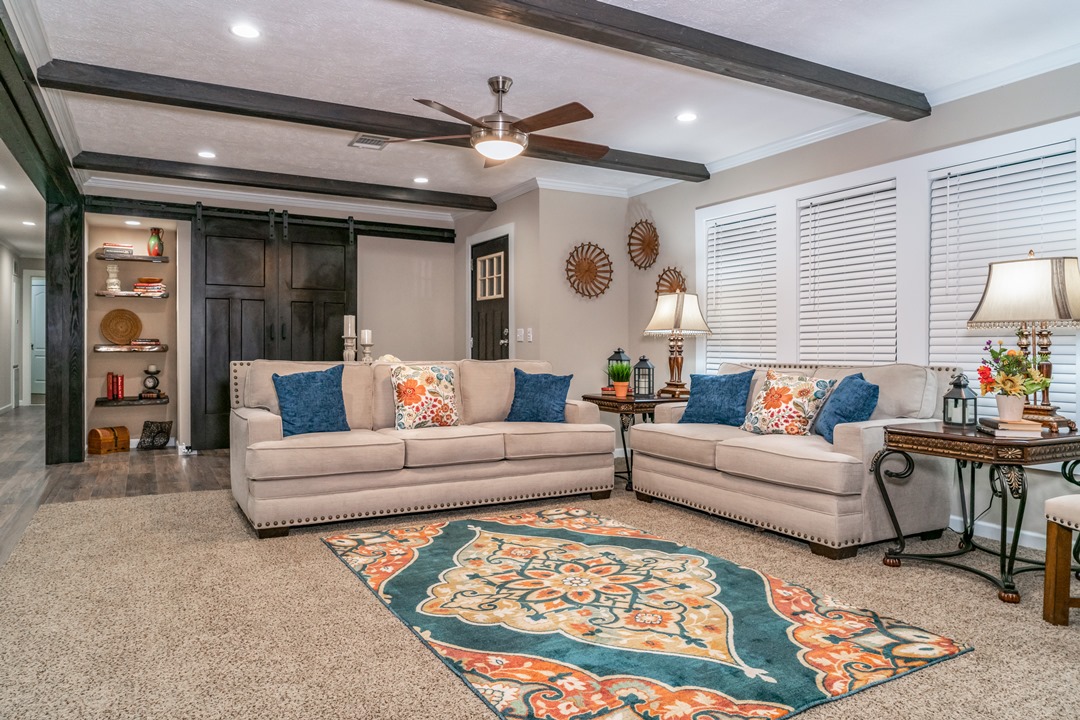 Cozy living room with two beige sofas adorned with colorful pillows. A vibrant patterned rug lies on the carpet, under soft lighting from two table lamps.
