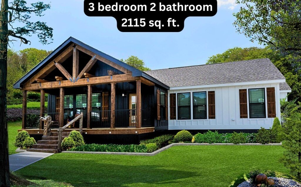 Stunning 3 bedroom, 2 bathroom manufactured home with 2115 sq. ft., featuring a rustic lodge-style covered porch with exposed wooden beams and stone steps, a dark exterior with white siding accents, and a beautifully landscaped yard with lush green grass and manicured bushes under a clear blue sky.