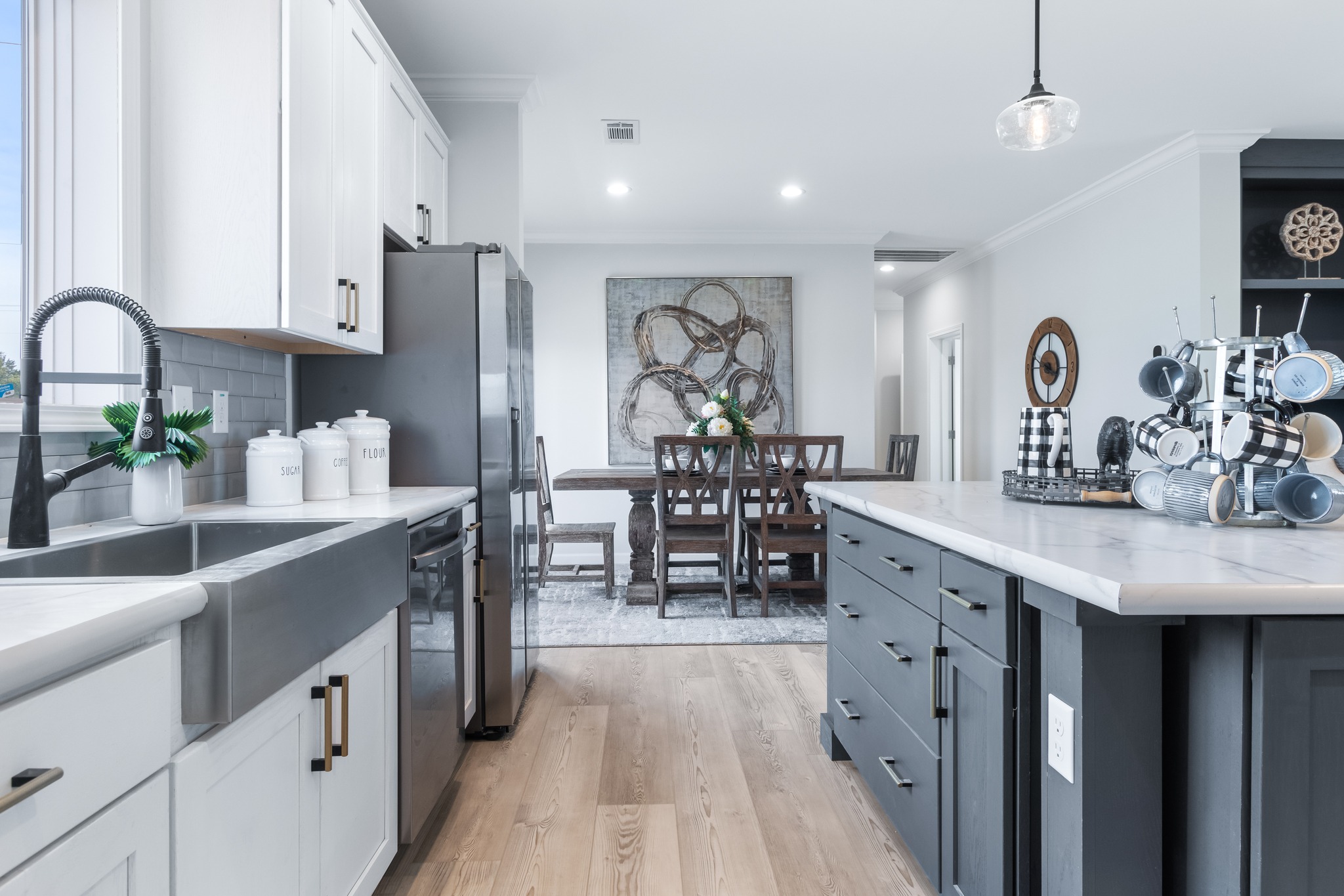 Modern kitchen and dining area with white cabinets, black island, and stainless steel sink. Wood floors and soft lighting create a cozy atmosphere.