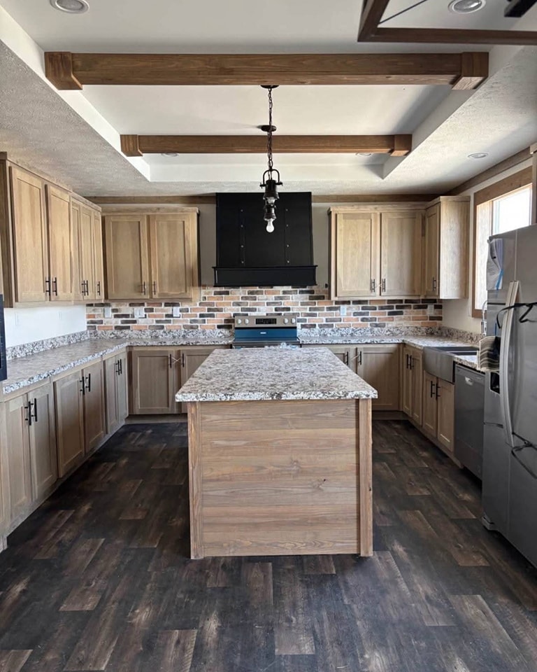 Rustic kitchen with wooden cabinets, granite countertops, and a central island. Brick backsplash, dark stove, and fridge create a warm, inviting atmosphere.