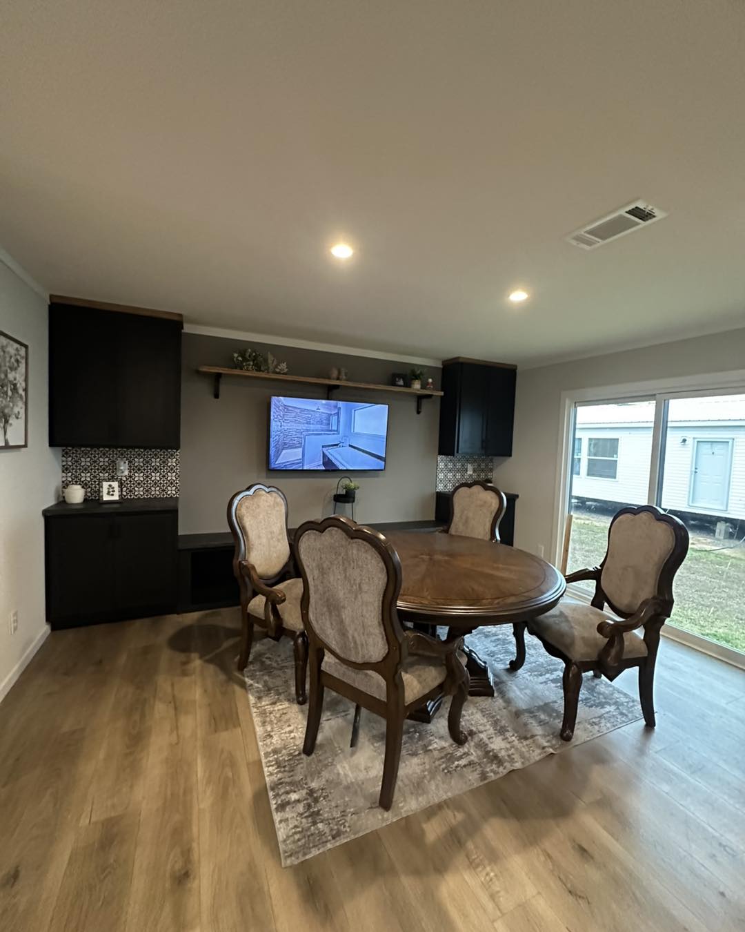 Cozy dining room with an elegant round wooden table and four upholstered chairs. A wall-mounted TV and decorative shelves create a warm, inviting atmosphere.